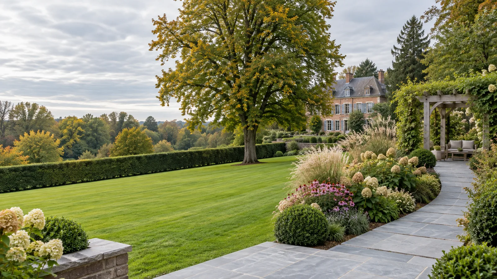 Pelouse anglaise descendante vers une haie de charmes taillée